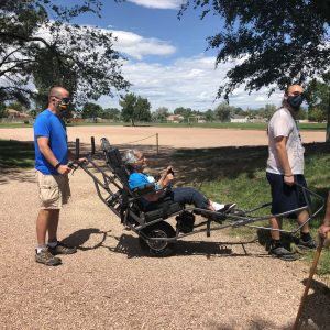 Two Men Helping to Wheel Person Across Grass